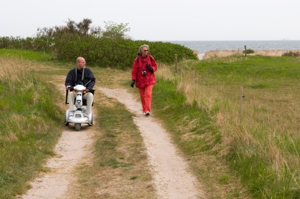 elderly man on a mobility scooter riding along a footpath