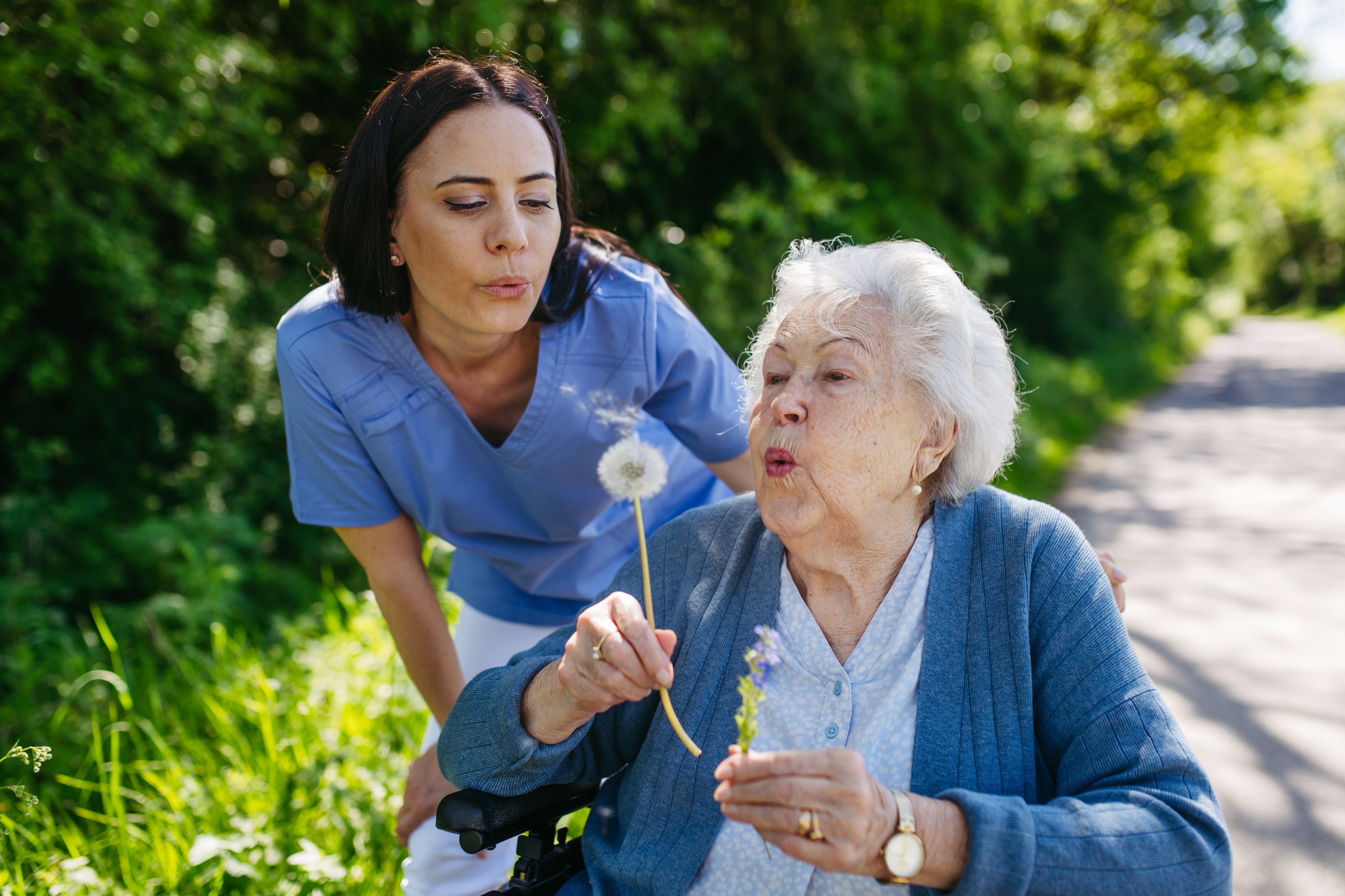 elderly woman with carer blowing a dandelion clock. 
